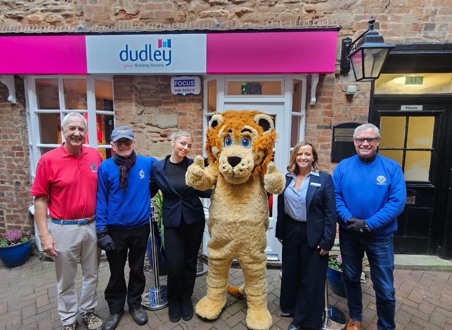 A person dress in a lion costume taking a picture with others next to savings branch